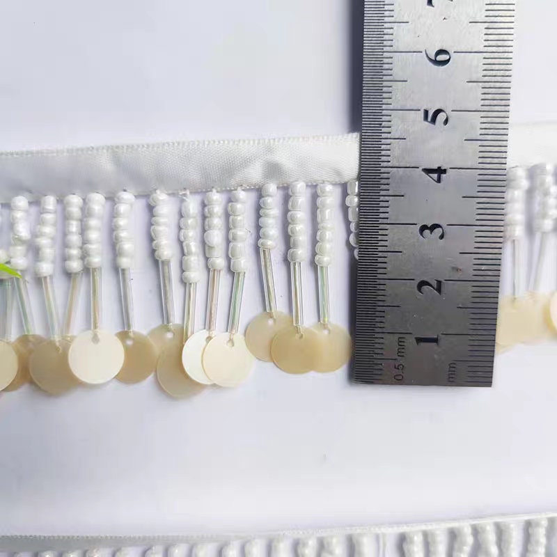 Handgemaakte kralenfranje van 90 cm lang en 3 cm breed, met zaadkralen en pailletten, in zwart, wit en beige.