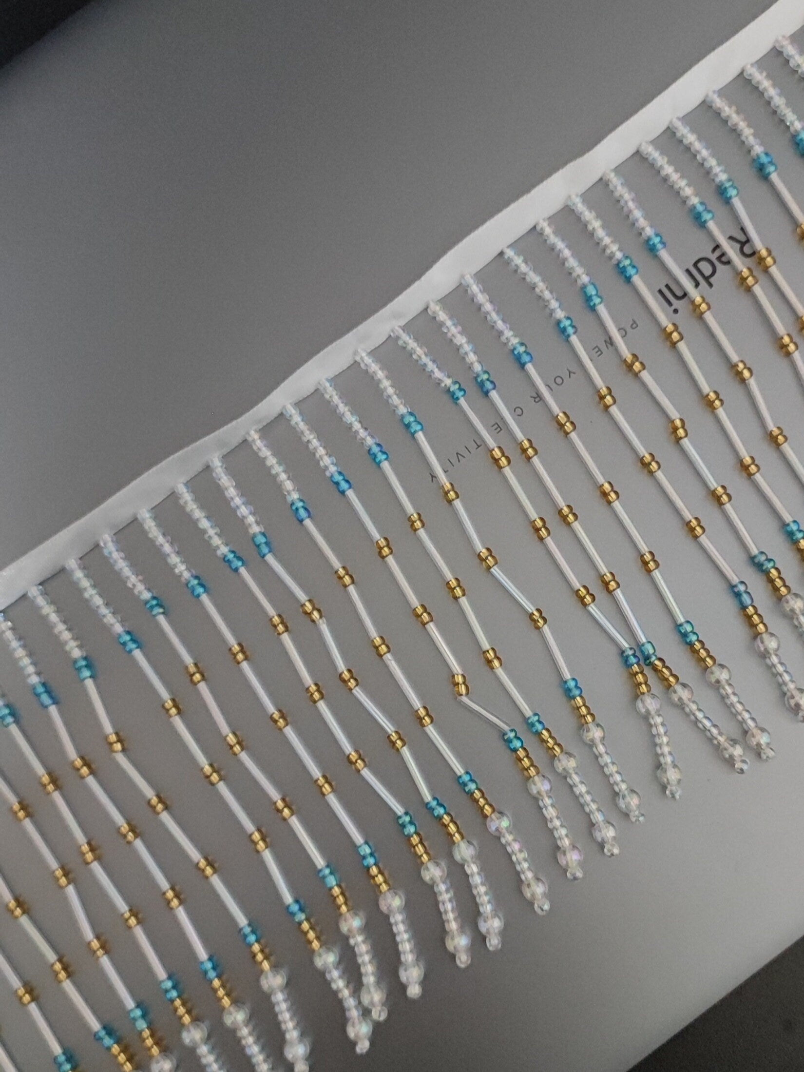 Handgemaakte lampenkapfranje van 90 cm lang en 11,5 cm breed met iriskralen in de kleuren helder, goud en turkooizen.