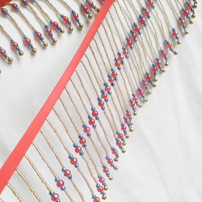 Frange perlée faite main, 90 cm de long x 10 cm de large, composée de perles rouges brillantes et de clochettes. Idéale pour abat-jour ou à réaliser soi-même.