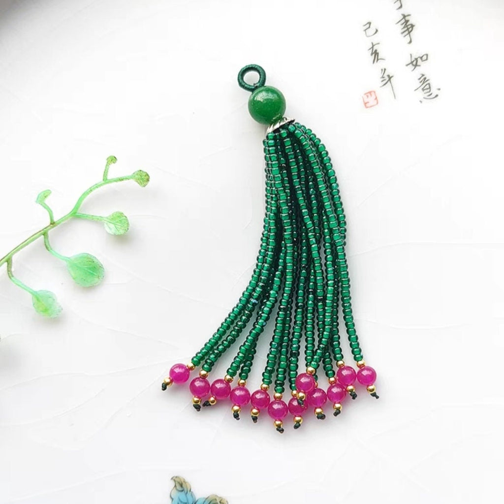 Perles artisanales de 8 à 9 cm de long, ornées de perles et de pierres précieuses émaillées, avec franges et pompons.