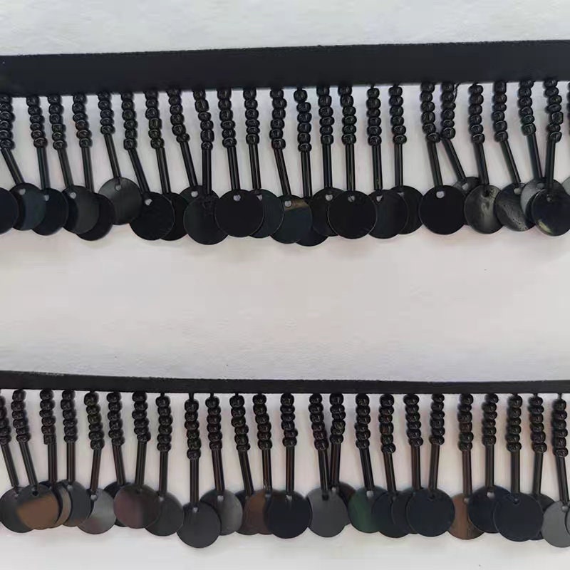 Handgemaakte kralenfranje van 90 cm lang en 3 cm breed, met zaadkralen en pailletten, in zwart, wit en beige.