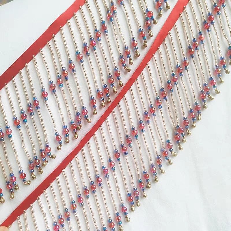 Frange perlée faite main, 90 cm de long x 10 cm de large, composée de perles rouges brillantes et de clochettes. Idéale pour abat-jour ou à réaliser soi-même.